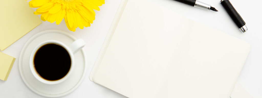Flat lay of a creative workspace with black coffee, a yellow daisy flower, a blank notebook, a pen, and sticky notes—the perfect setup for writing, journaling, or productivity.